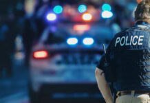 Gunfire Chaos: 10 DEAD, City on Edge! Police officer with patrol car and flashing lights.