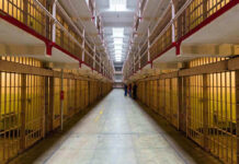 Torture Uprising – Prison Inmates Ignite Matresses! Long hallway with prison cells on both sides.
