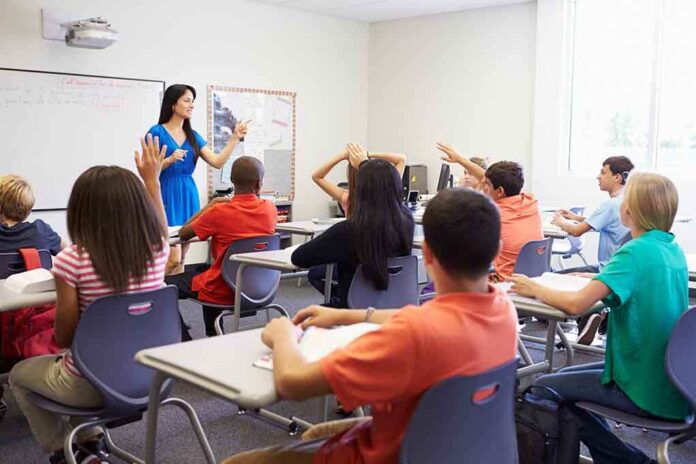 shutterstock_199144970 Teacher in a blue dress instructing students in a classroom with hands raised