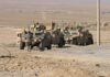 Two military humvees with soldiers in a desert landscape