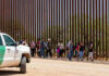 People walking beside tall fence and border patrol vehicle.