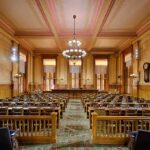 Kirk Assassin’s Attorney Pull Outrageous Courtroom Stunt! Interior view of a historic courtroom with wooden furnishings and chandeliers