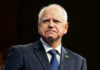 Tim Walz Just Pardoned WORST of the WORST Illegal Alien! Man in suit with a U.S. flag pin.