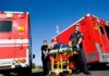 Paramedics move a patient on a stretcher between red ambulances