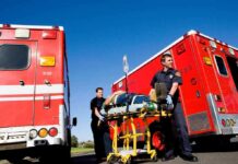 Paramedics move a patient on a stretcher between red ambulances