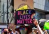 BLM Riots Erupt Right in Time For The Midterms protester holds colorful sign at a city street demonstration