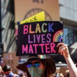 BLM Riots Erupt Right in Time For The Midterms protester holds colorful sign at a city street demonstration