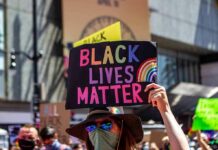 BLM Riots Erupt Right in Time For The Midterms protester holds colorful sign at a city street demonstration