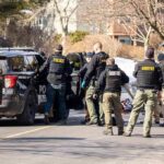 Police and sheriff officers gather around vehicles on a suburban street