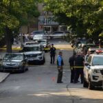 Police officers secure a residential street with patrol cars and yellow tape