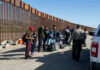 DHS Responds to Latest Migrant Caravan Marching Toward US Border Group of people standing by a border fence with officers and vehicles