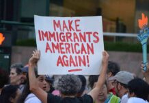 Troubling Anti-Ice Message Written at ICE Shooting Site Teddy Williams at a protest holding a sign reading 'Make Immigrants American Again'
