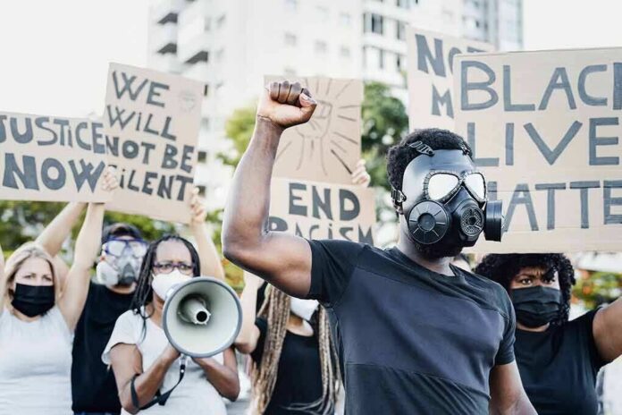 shutterstock_1767306362 Protester in gas mask raises fist during street demonstration