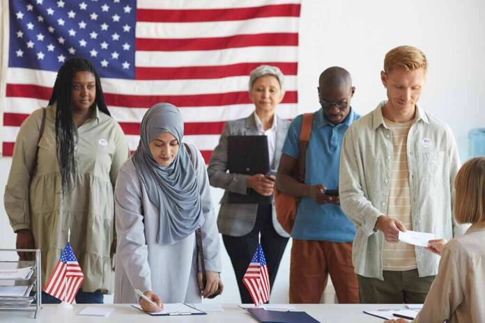 shutterstock_1810358971 Voters standing in line at a polling station with a U.S. flag