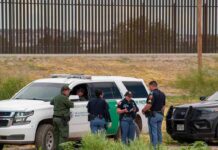 law enforcement officers confer beside patrol vehicles near a border fence