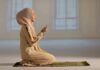 Woman in hijab praying on a mat indoors