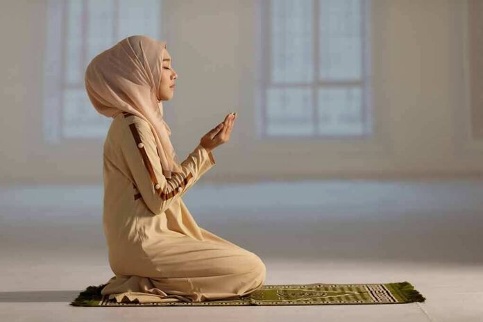 shutterstock_2084286106 Woman in hijab praying on a mat indoors
