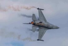 F-16 CRASHES Over Michigan, Pilot Vanishes in Fireball Fighter jet banking with afterburner against a cloudy sky