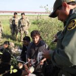 Border agents detain a group of migrants in a grassy field