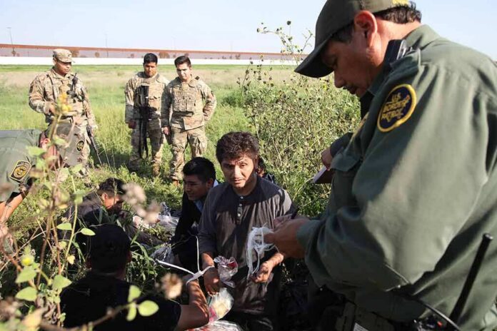 Border agents detain a group of migrants in a grassy field