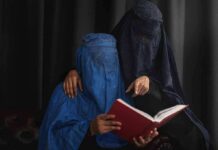 Two veiled women reading a red book together