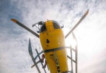 Yellow helicopter seen from below with spinning rotor against a bright sky