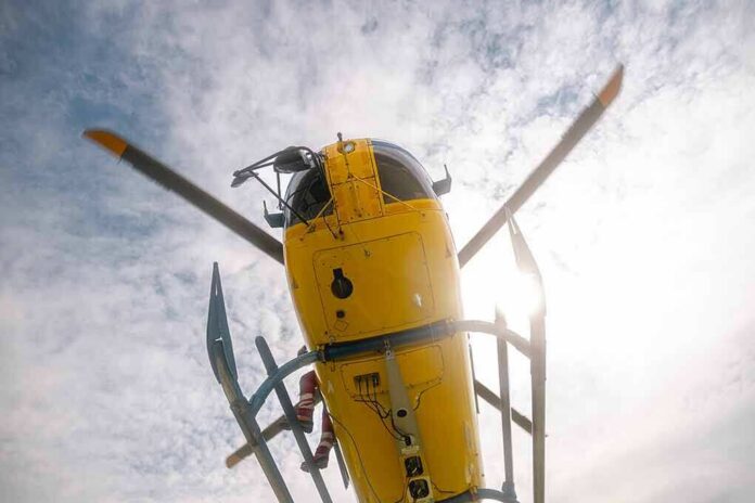 Yellow helicopter seen from below with spinning rotor against a bright sky
