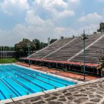 Olympic-size outdoor swimming pool beside empty stadium bleachers