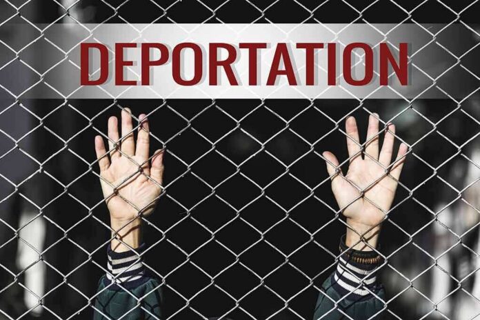 Hands gripping chain-link fence with deportation sign