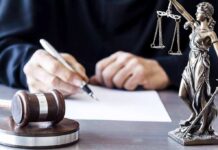 Trump Aide Slaps Restraining Order On Congressman Judge writing at desk with gavel and Lady Justice statue