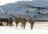Curfew Imposed on US Bases After Marine Arrested Soldiers disembark and walk past a large military helicopter