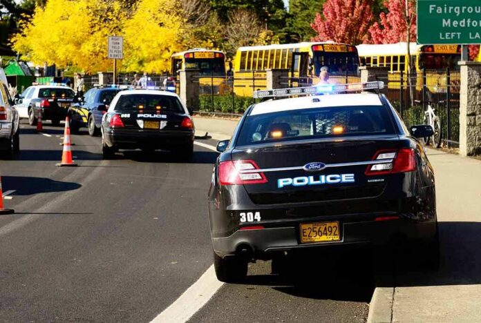 shutterstock_117302929-1 Police cars with flashing lights near school buses on a city street