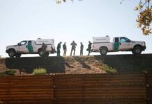 Border patrol agents stand between two marked trucks on an embankment