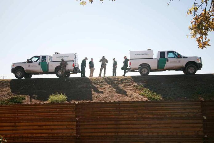 shutterstock_1243518340 Border patrol agents stand between two marked trucks on an embankment