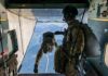 Paratroopers jump from a military aircraft over coastline