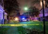 Police car blocks residential street at night behind caution tape
