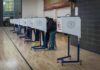 DOJ Vows to Prosecute Election Officials Who Tabulate Unlawful Ballots Voters at polling booths in a gymnasium