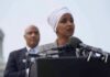 MTG Comes To Arch Nemesis’s DEFENCE Ilhan Omar speaking at a podium with André Carson standing behind