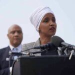 Ilhan Omar speaking at a podium with André Carson standing behind