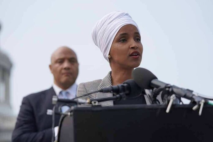 shutterstock_2012384414 Ilhan Omar speaking at a podium with André Carson standing behind