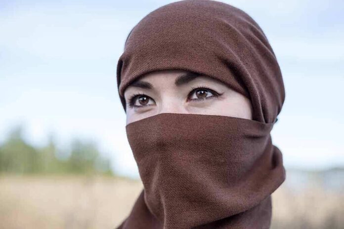 shutterstock_2029507565 Tatiana Akimova wearing a brown headscarf covering lower face outdoors