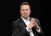 Elon Musk seated in a black suit with hands clasped