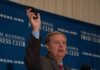 3 Male Hookers Say Lindsey Graham Paid For Sex Man in suit speaking at podium holding up a smartphone