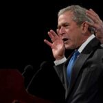 George W. Bush speaking at a podium with hands raised
